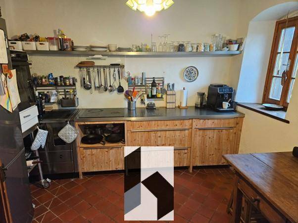 Rustikale Küche mit Holzschränken, Metallarbeitsplatte und Terrakotta-Fliesenboden.