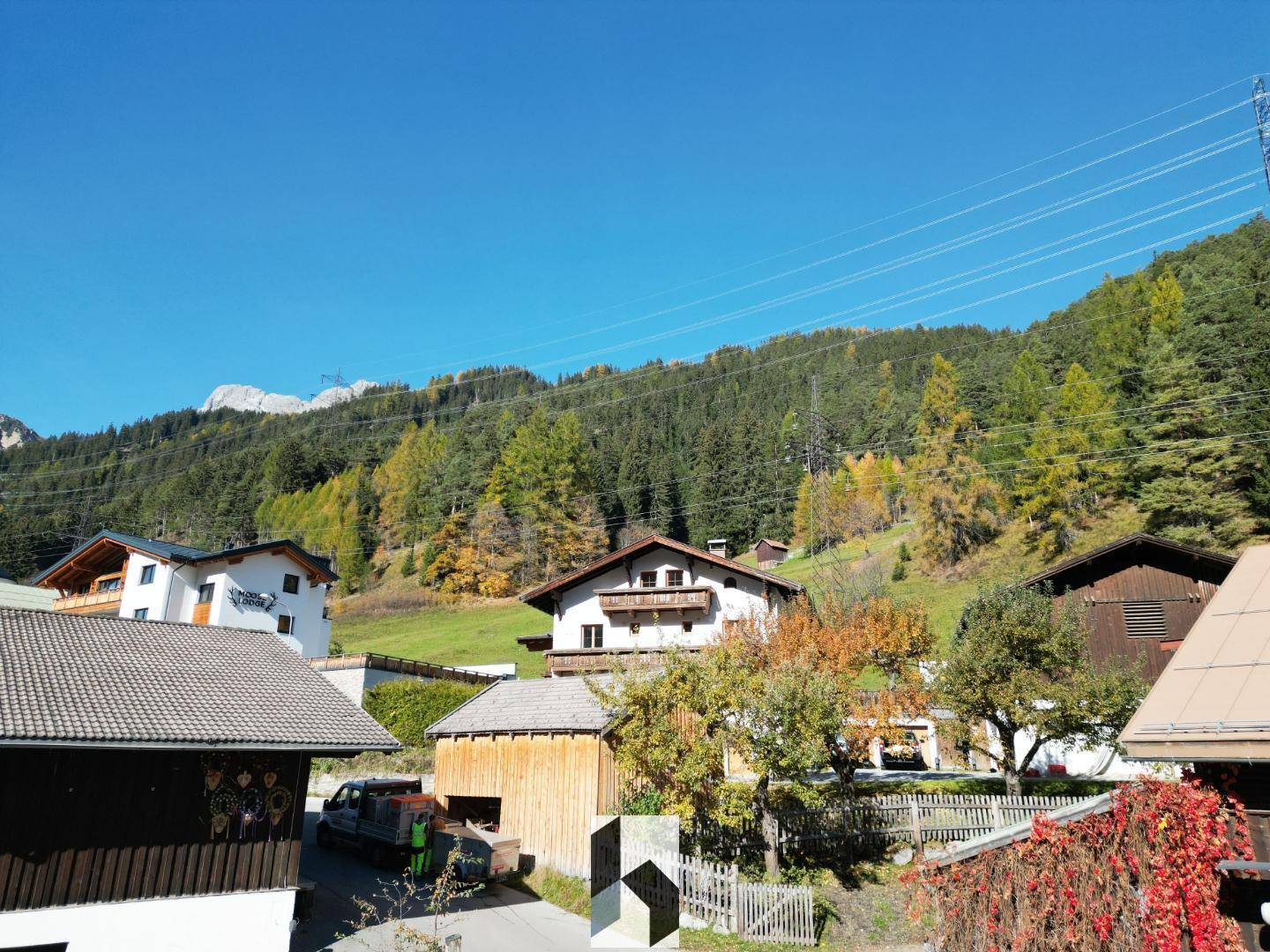 Blick auf die ländliche Umgebung mit traditionellen Häusern und einem bewaldeten Hügel unter blauem Himmel.