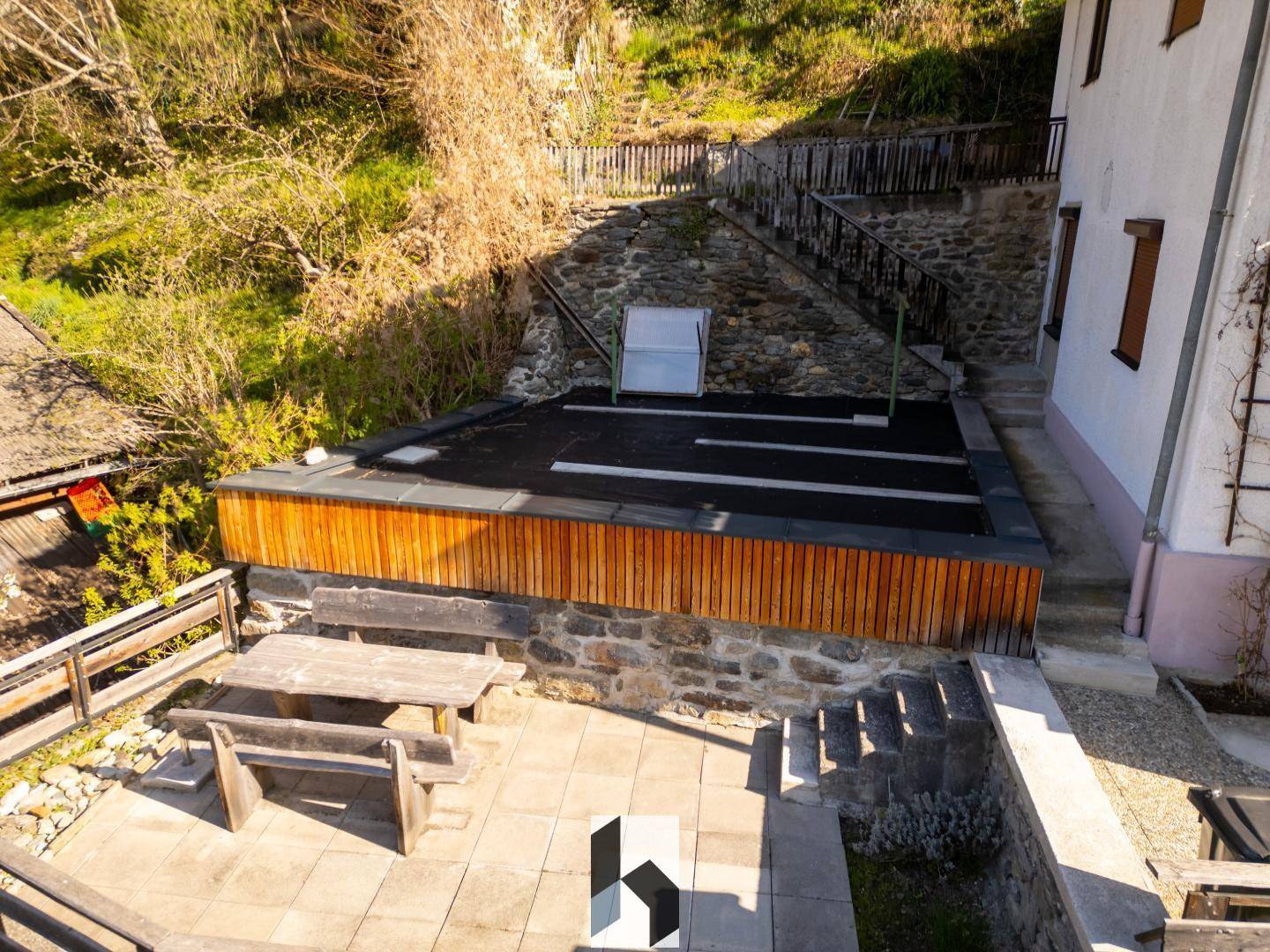 Gepflasterte Terrasse mit Holzbänken und Tisch, umgeben von Natur und Steinmauern, ideal zum Entspannen.
