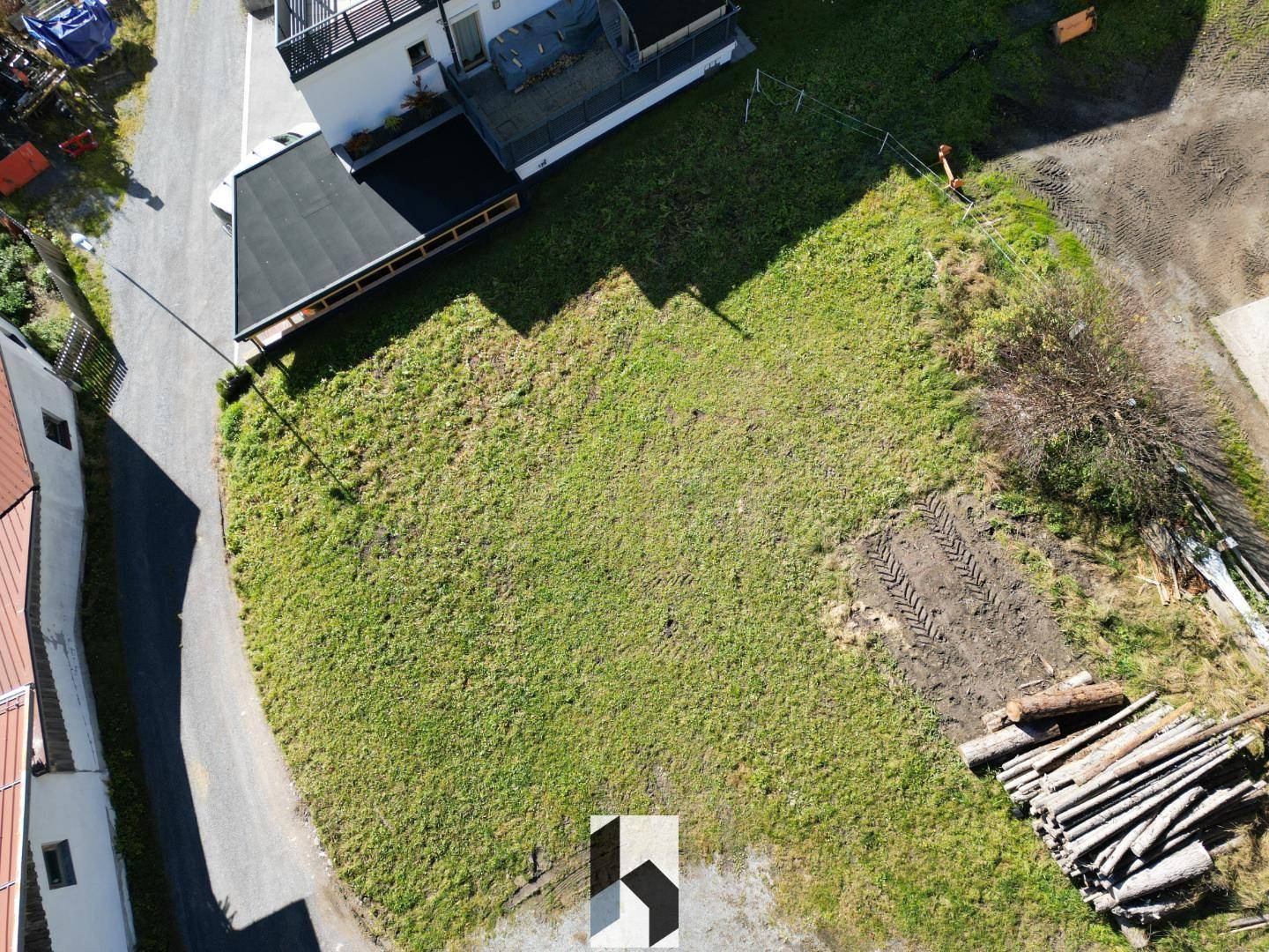 Übersicht des Grundstücks von oben mit angrenzendem Gebäude und einem Holzstapel am Rand.