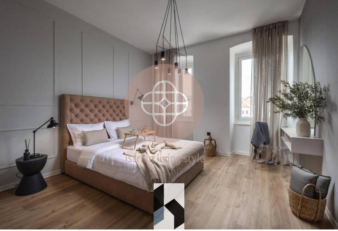 Helles Schlafzimmer mit großem gepolstertem Bett, Holzboden und hohen Fenstern.
