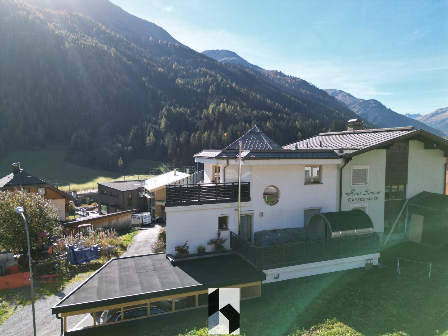 Gebäudeansicht mit moderner Architektur, Balkonen und einem Whirlpool im Freien vor Bergkulisse.