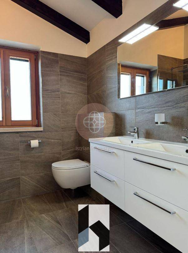 Geräumiges Badezimmer mit Doppelwaschbecken, großem Spiegel und dunklen Fliesen.