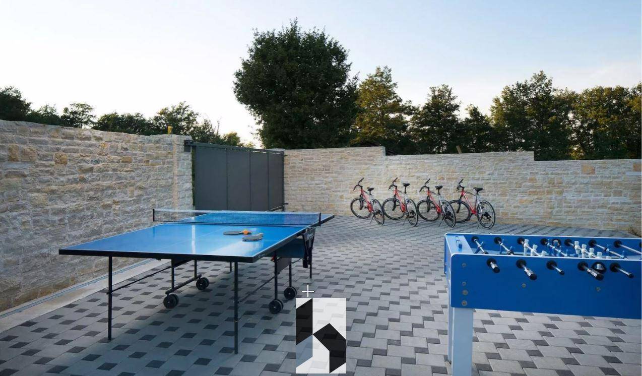 Outdoor-Spielbereich mit Tischtennisplatte, Kicker und Fahrrädern vor einer Steinmauer.