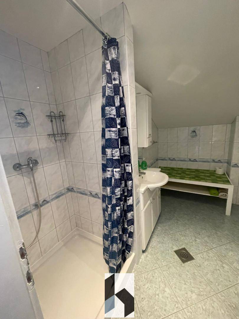 Badezimmer mit Dusche, weißen Fliesen, Einzelwaschbecken und Dachschräge.