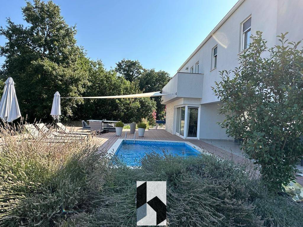 Sonnige Poolterrasse umgeben von mediterraner Bepflanzung und altem Baumbestand.