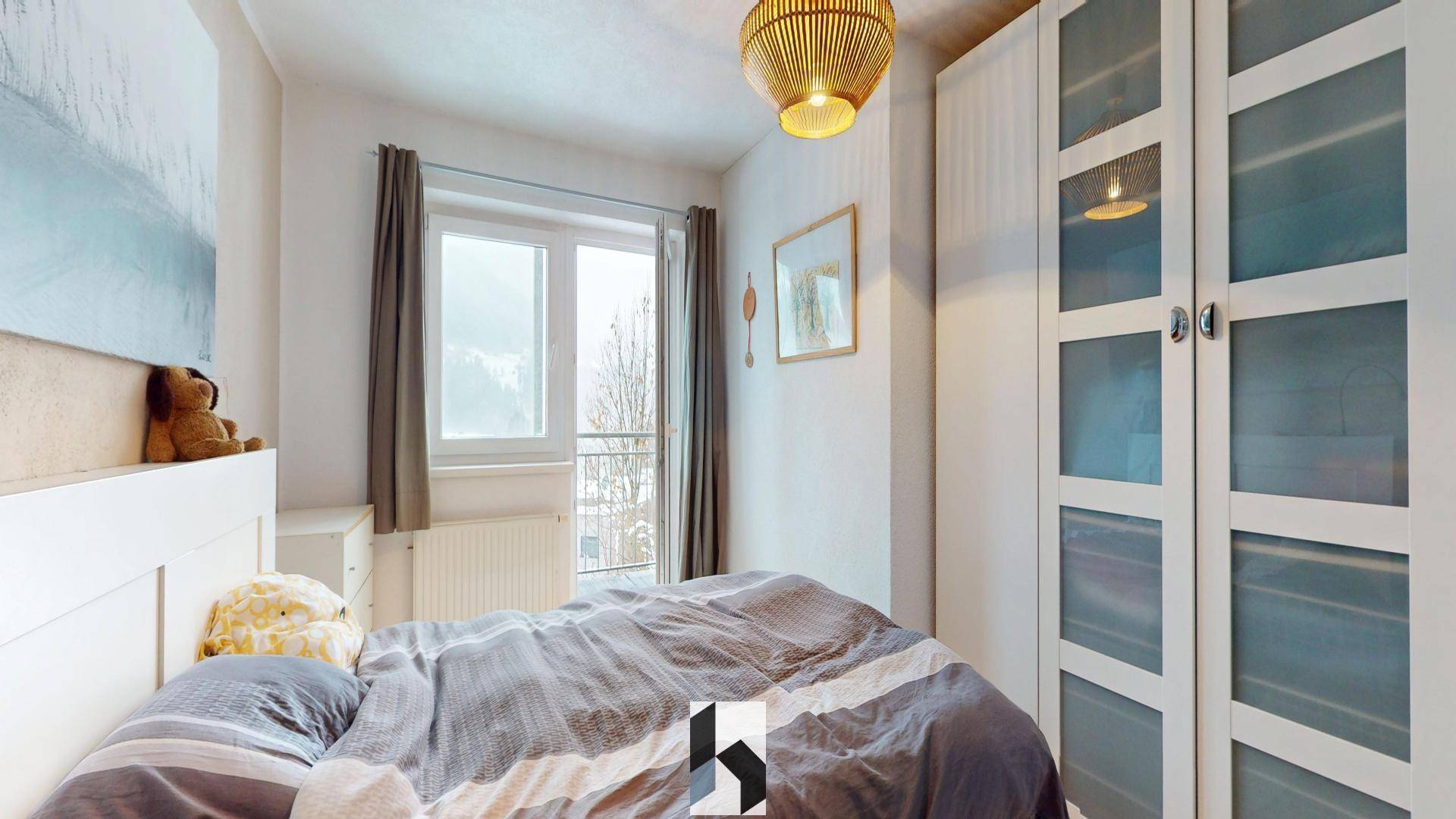 Helles Schlafzimmer mit Doppelbett, Kleiderschrank und Blick auf die verschneite Landschaft.