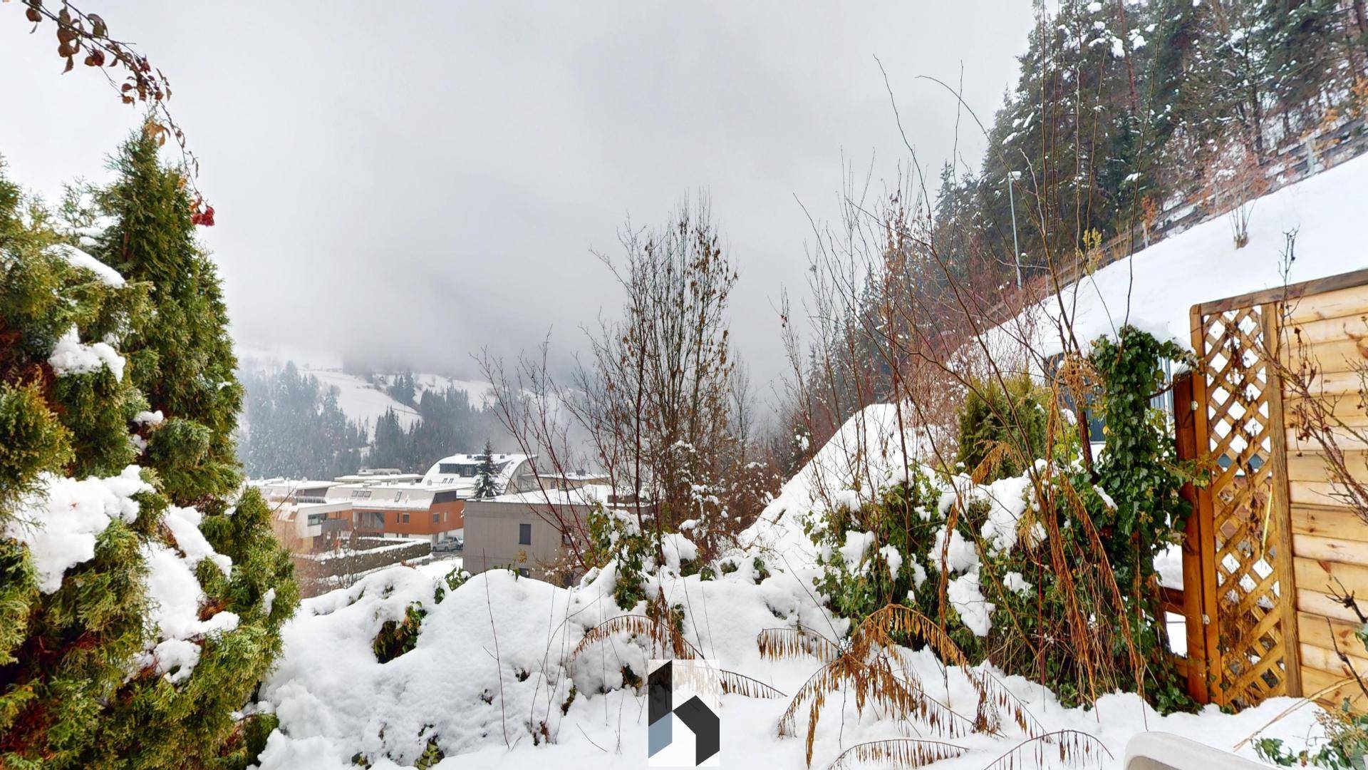 Verschneite Gartenlandschaft mit Bäumen und Blick auf die umliegenden Häuser.