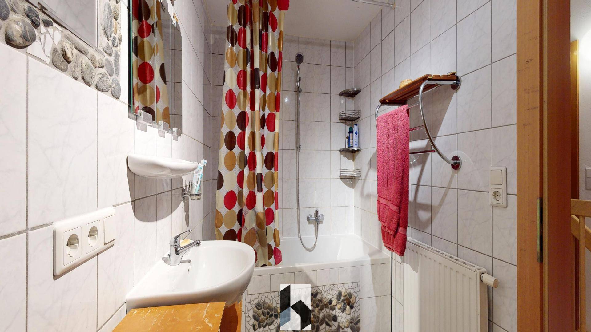 Gefliestes Badezimmer mit Badewanne, Duschvorhang und Einzelwaschbecken.