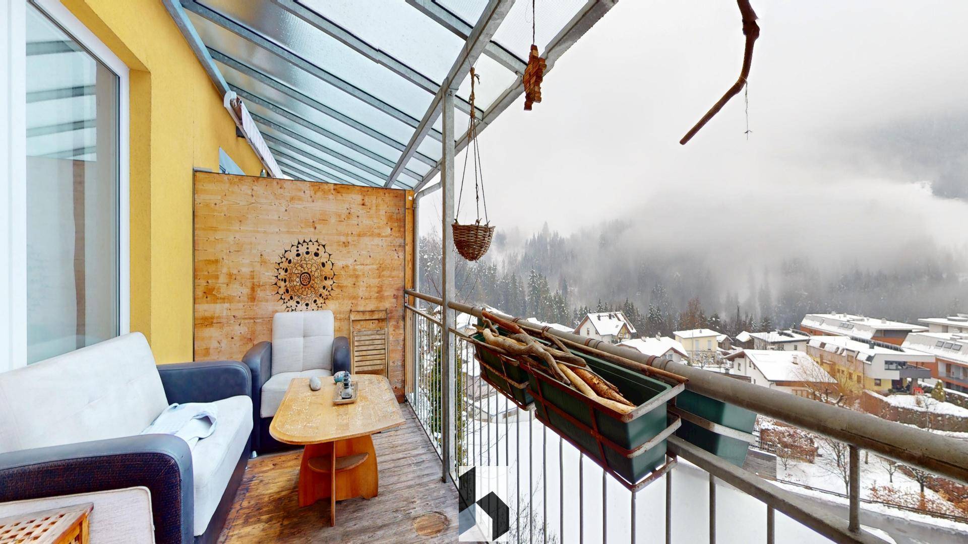 Verglaster Balkon mit Sitzgelegenheiten und weitem Blick auf die verschneite Berglandschaft.