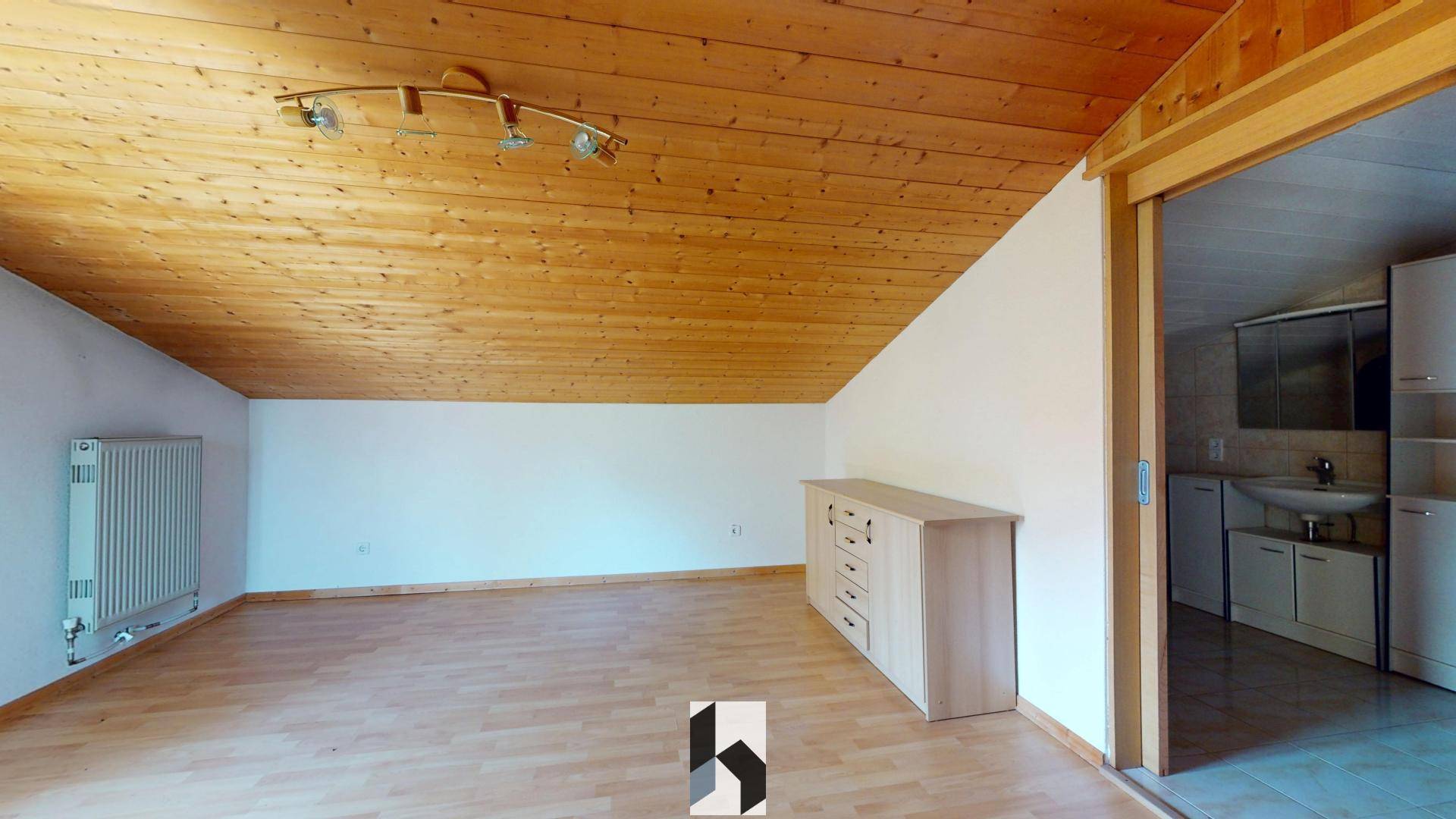 Dachgeschossraum mit Holzdecke, Parkettboden und Heizkörper.