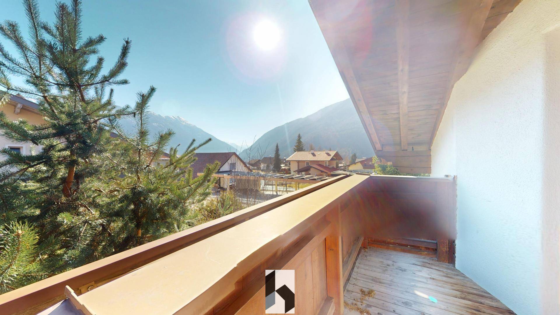 Sonniger Balkon mit Holzboden und weitem Blick auf die umliegenden Berge.