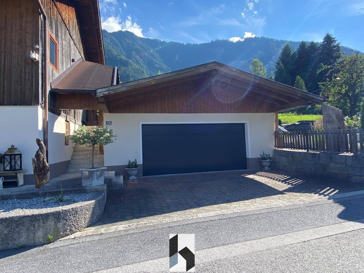 Doppelgarage mit Carport und gepflasterter Zufahrt vor dem Haus.