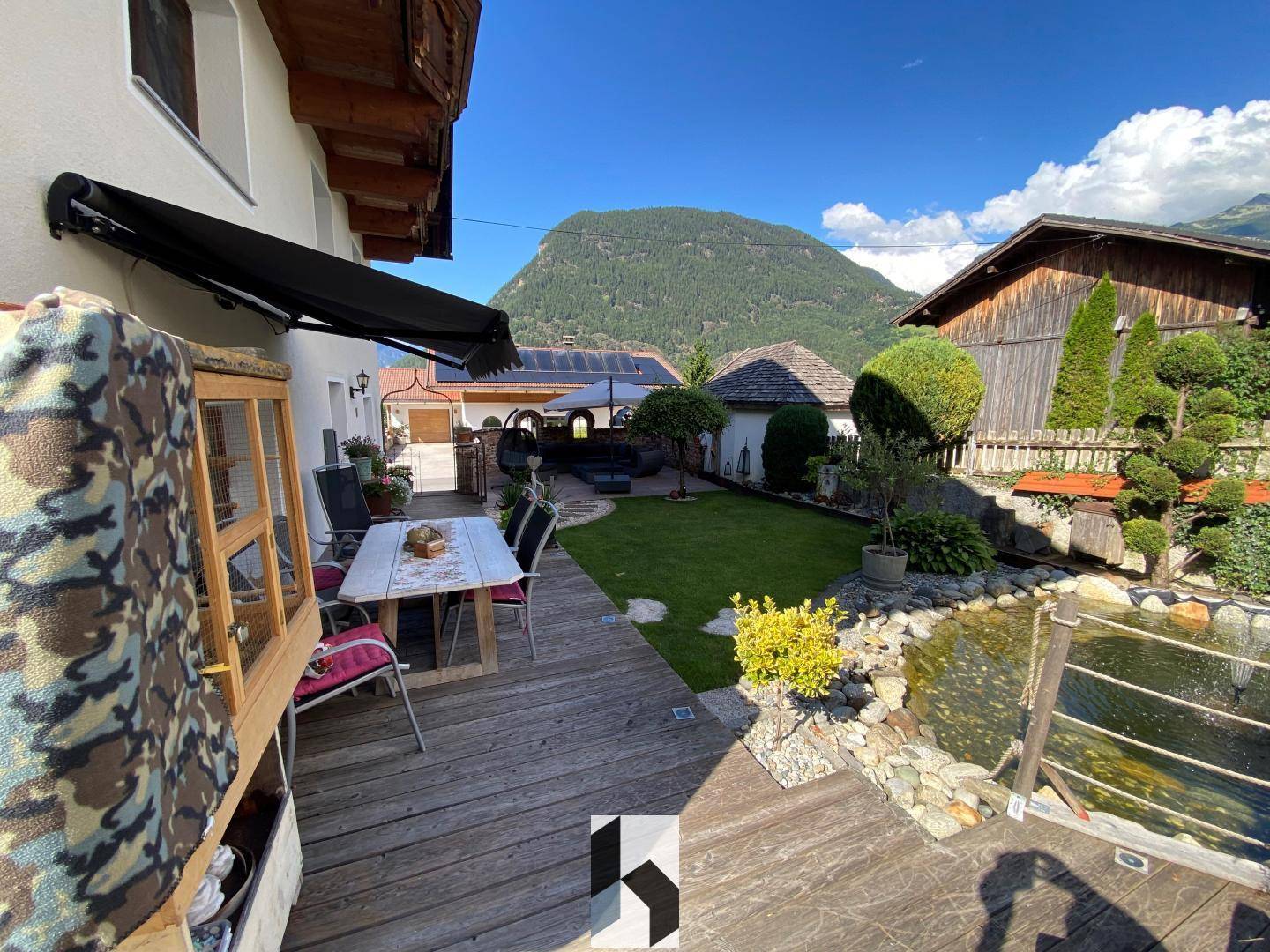 Gepflegter Garten mit Holzterrasse, Teich und Bergblick.