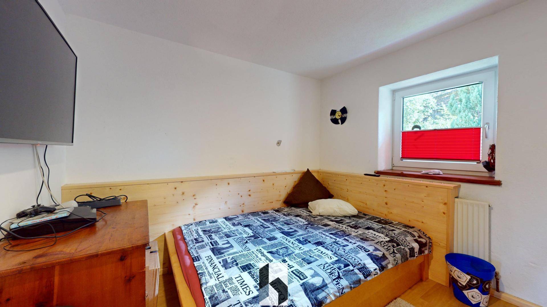 Schlafzimmer mit Holzbett, Holzboden und Fenster mit Blick ins Grüne.