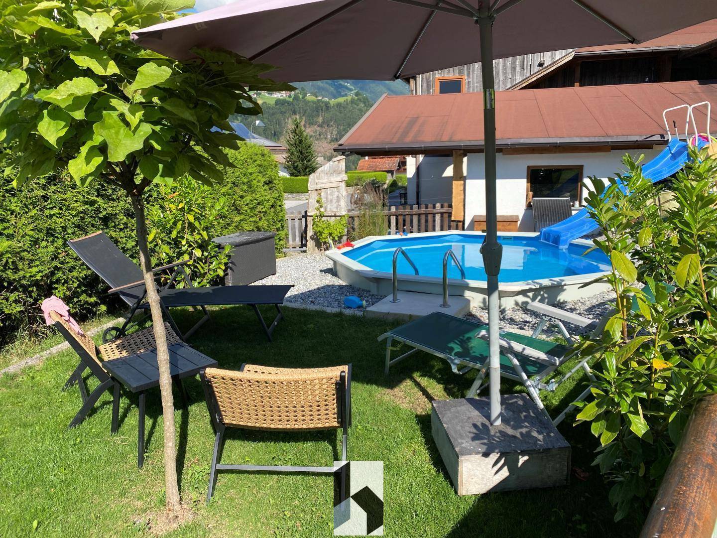 Gartenbereich mit Aufstellpool, Liegestühlen und schattenspendendem Baum.
