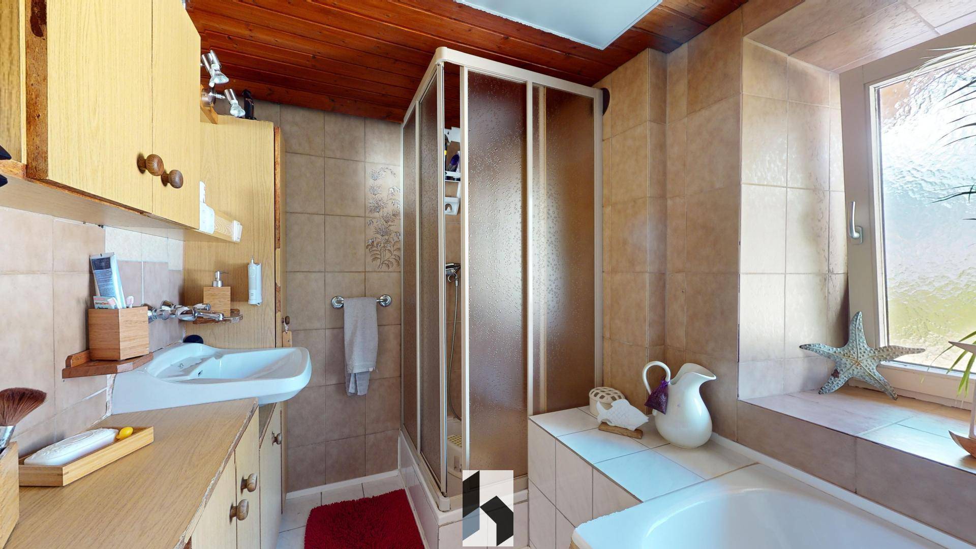 Badezimmer mit Dusche, Badewanne, Fenster und beigefarbenen Fliesen.