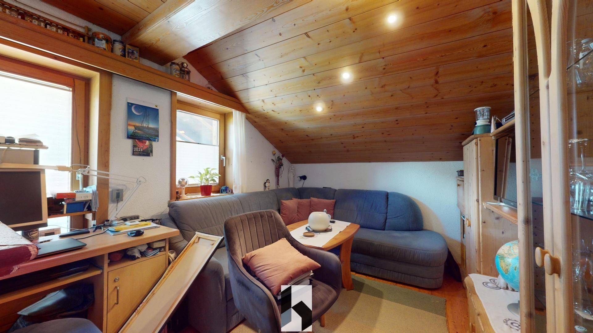 Wohnzimmer im Dachgeschoss mit Holzbalkendecke, Sofa und Stauraum.