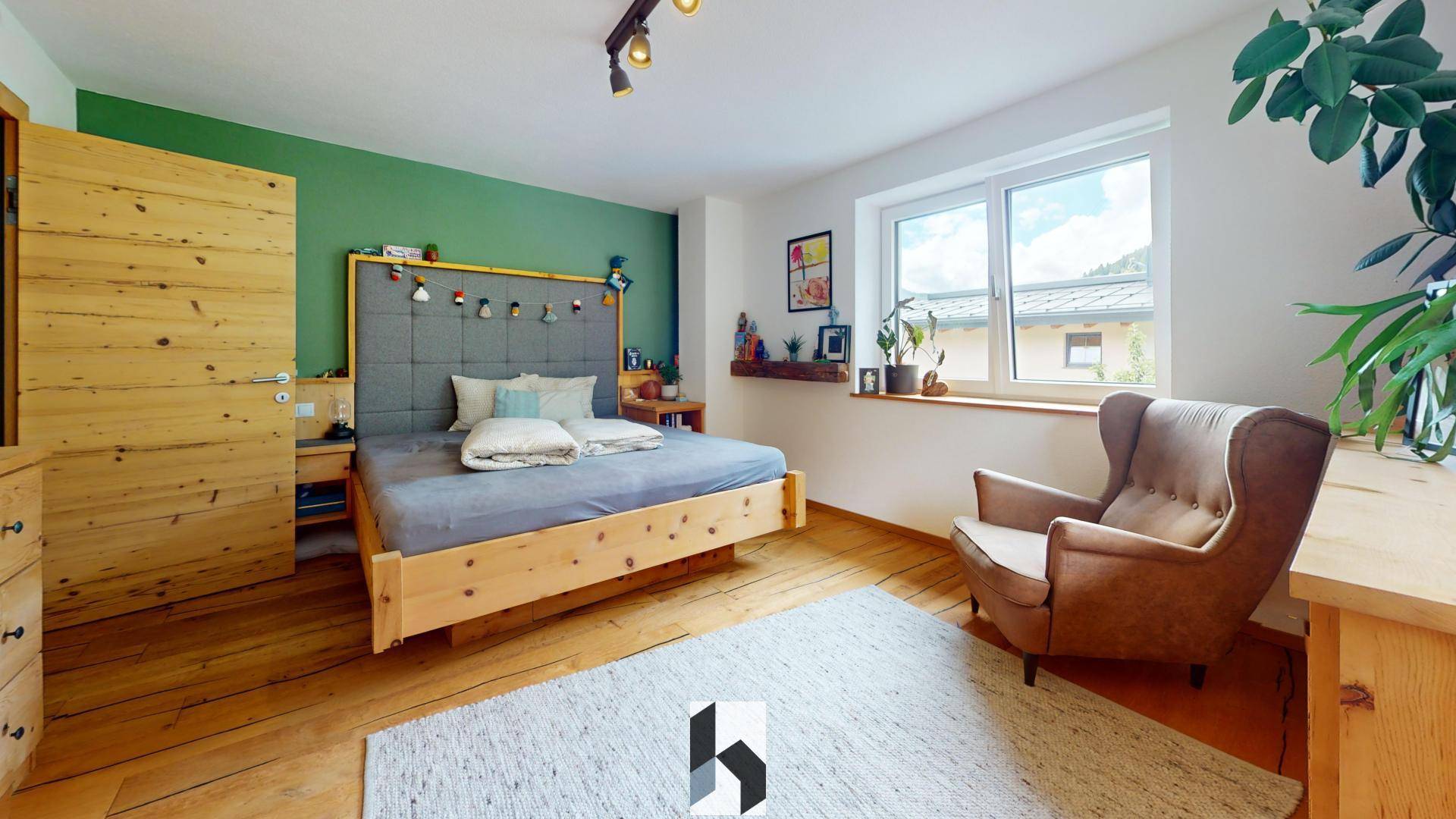 Helles Schlafzimmer mit Holzbett, grüner Akzentwand und bequemen Sessel.