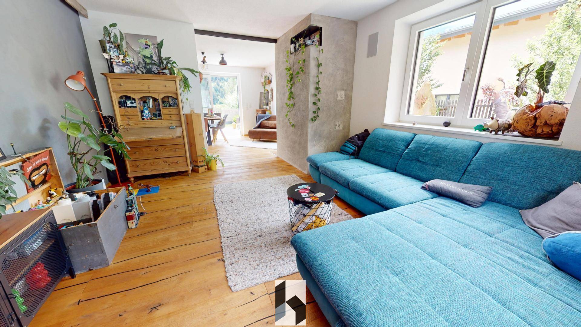 Gemütliches Wohnzimmer mit blauem Ecksofa, Holzboden und rustikalen Möbeln.