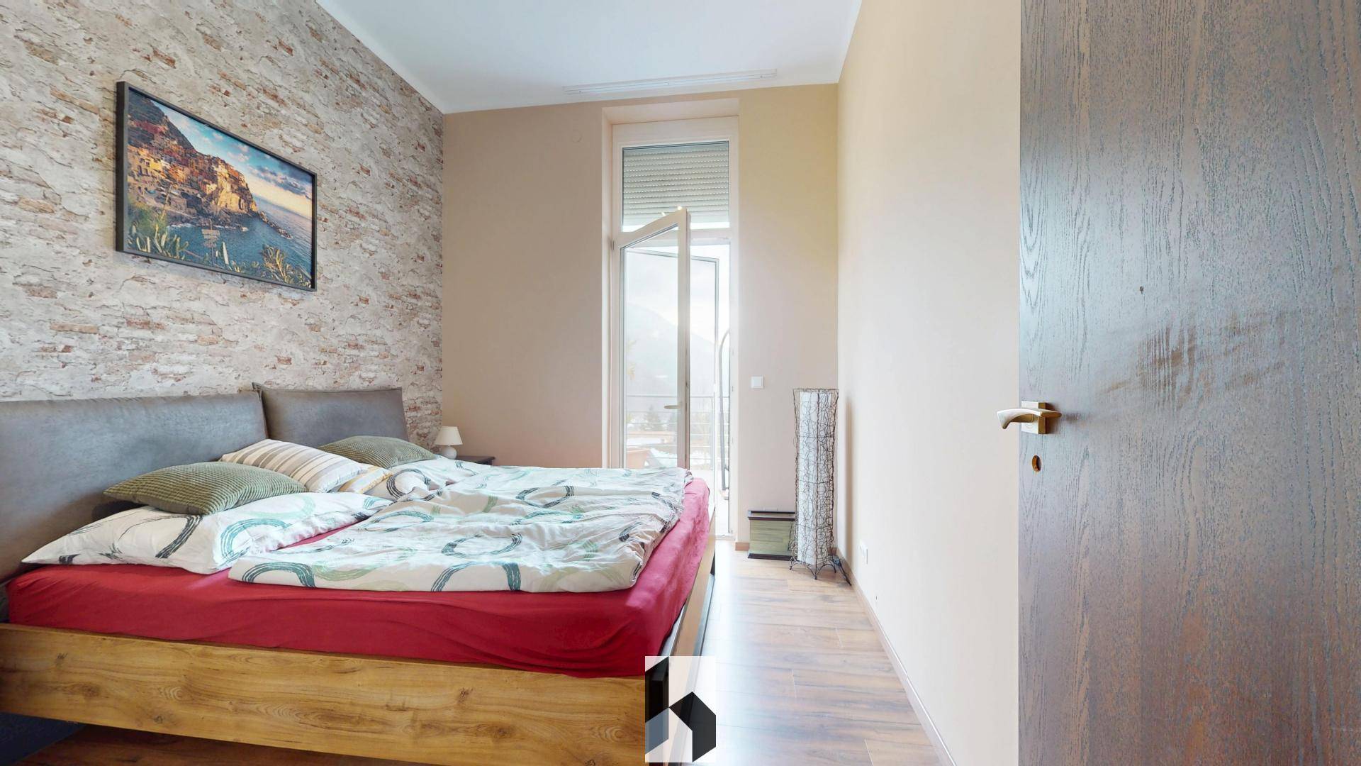 Gemütliches Schlafzimmer mit Holzbett, freigelegter Ziegelwand und Zugang zu einem kleinen Balkon oder einer Terrasse.