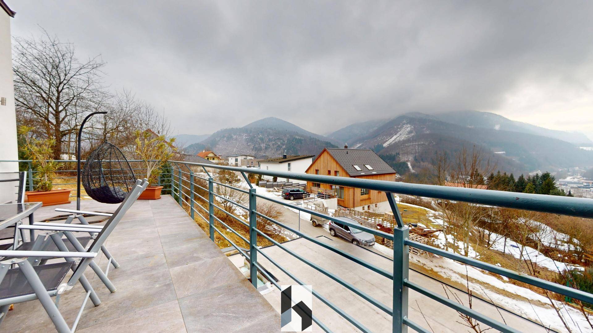 Großer Balkon mit Sitzgelegenheiten und einem weiten Panoramablick auf die umliegende Berglandschaft und das Tal.