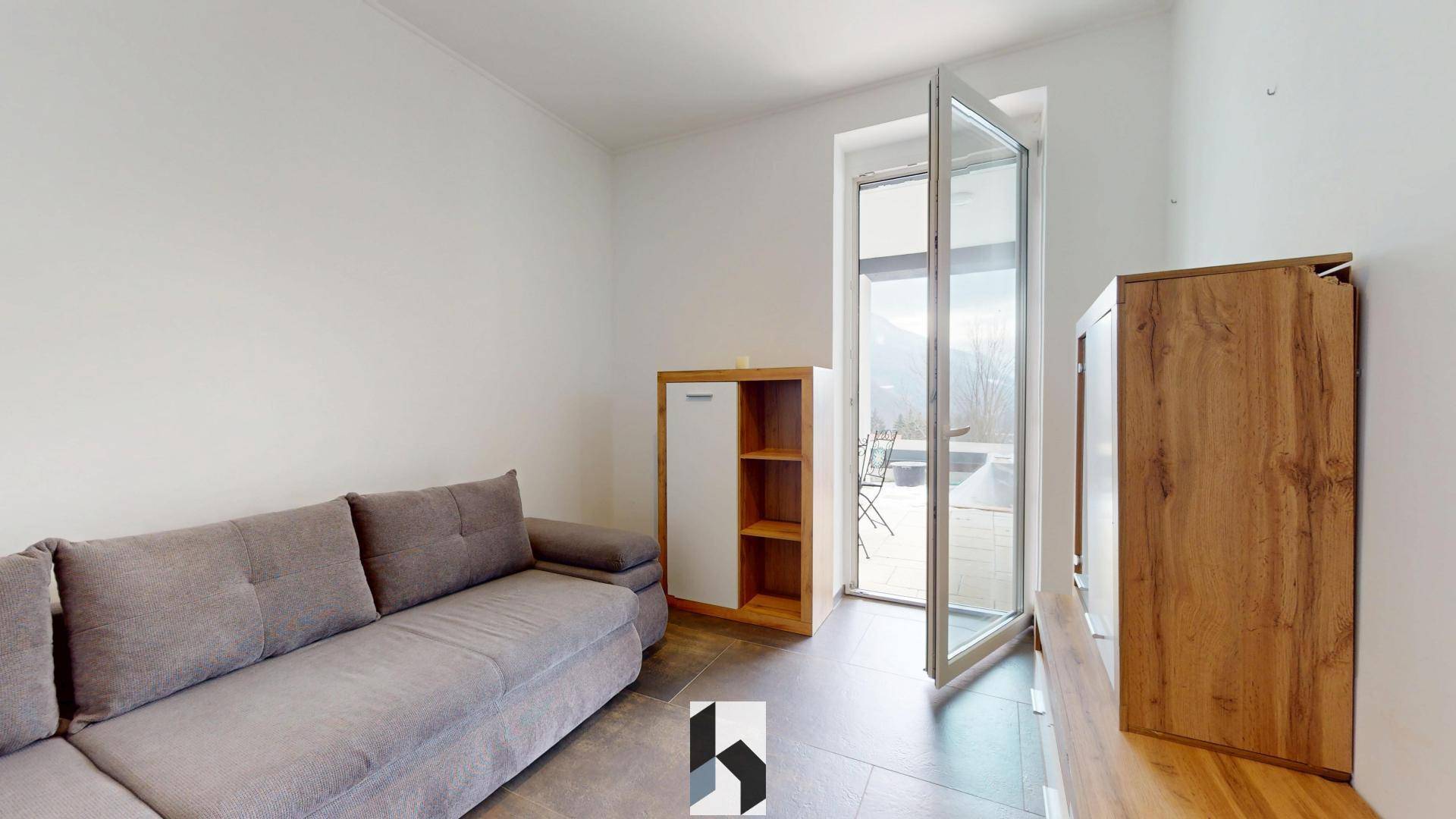 Heller Wohnbereich mit Sofa, modernen Möbeln und großen Glastüren, die zu einer Terrasse mit Bergblick führen.