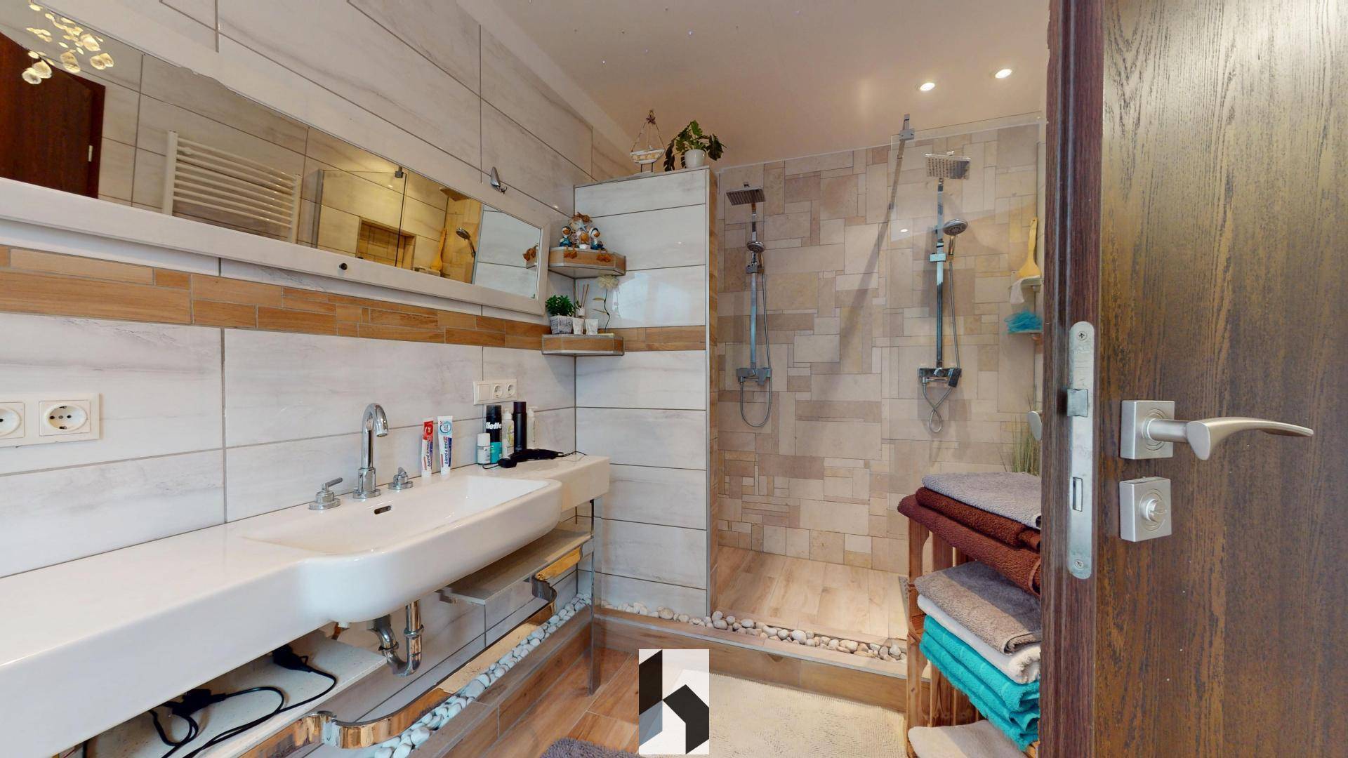Geräumiges Badezimmer mit begehbarer Dusche, Doppelwaschbecken und großem Spiegel, gefliest mit Holzdetails.