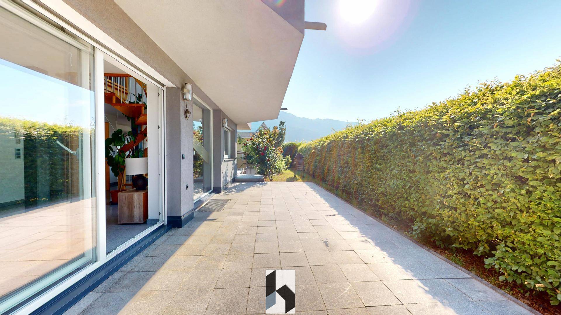 Sonniger Terrassenbereich mit Steinplatten und hoher Hecke für Privatsphäre.