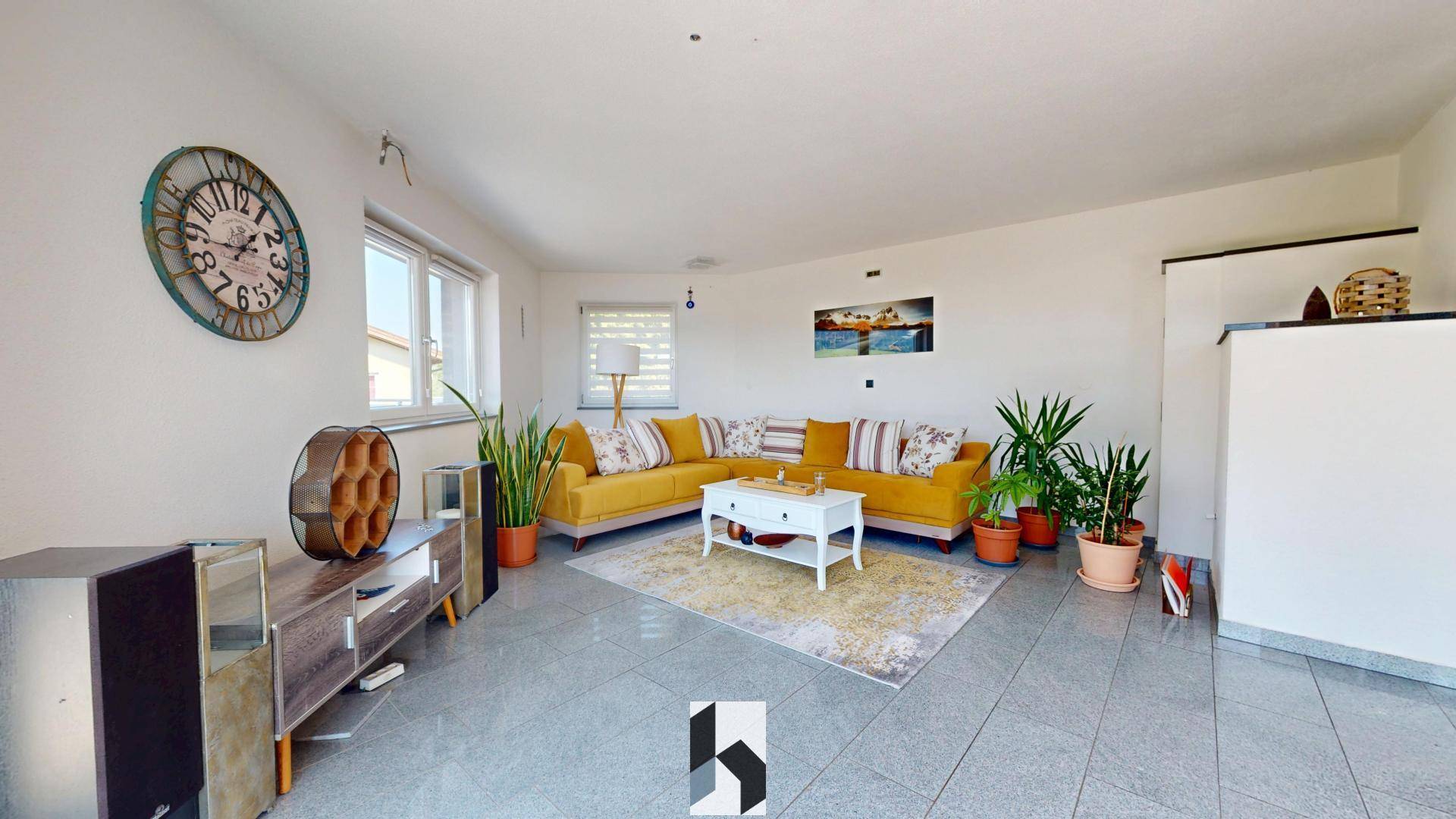 Gemütliches Wohnzimmer mit gelbem Sofa, vielen Pflanzen und hellem Fliesenboden.