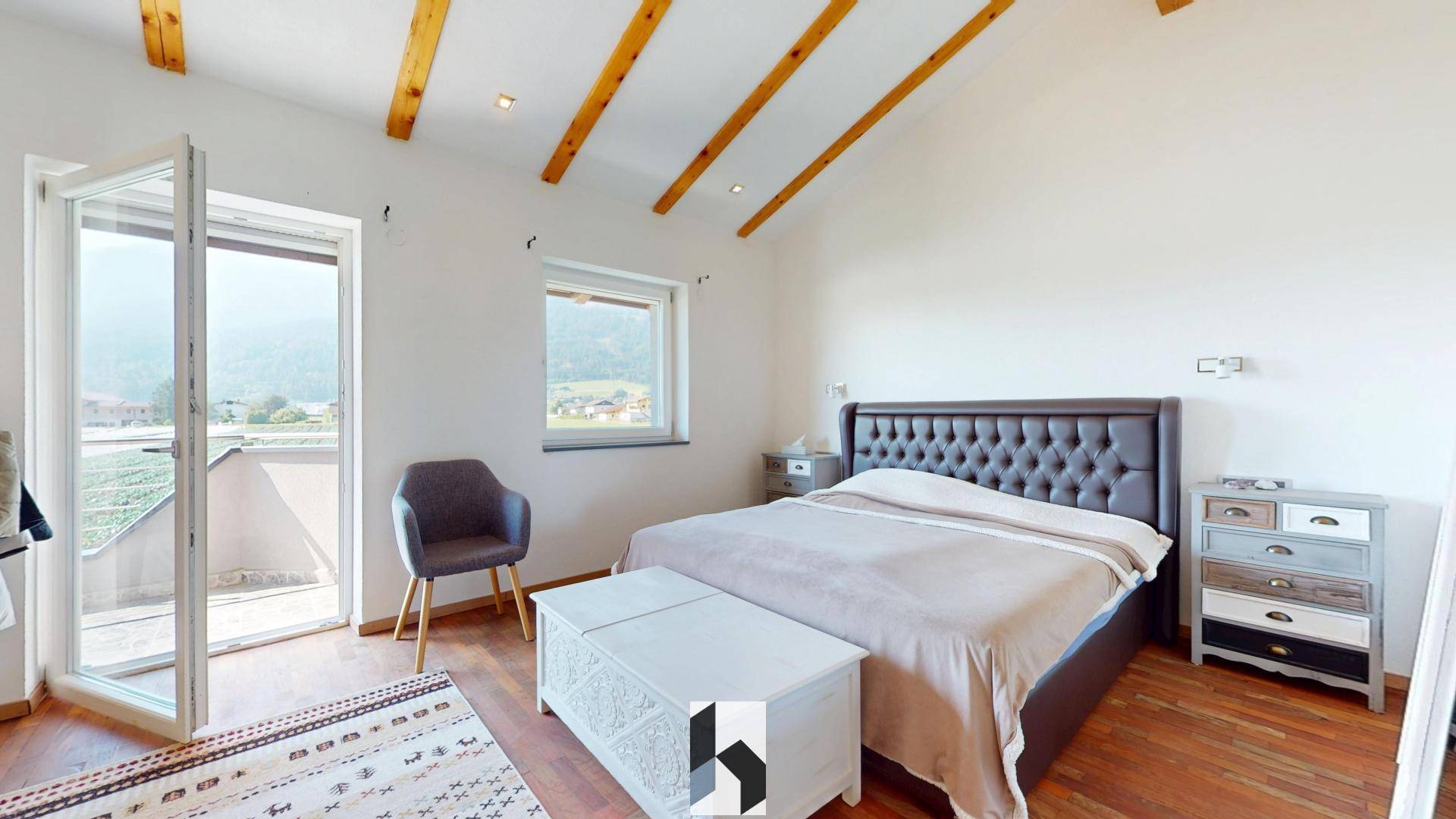 Helles Schlafzimmer mit Holzbalken, großem Bett und Zugang zum Balkon.