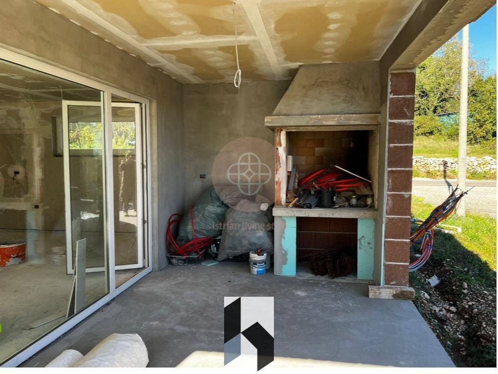 Überdachte Terrasse im Rohbau mit eingebautem Grill und großen Glasschiebetüren.