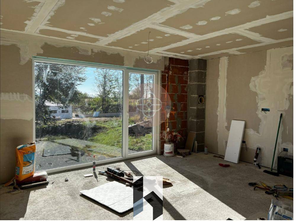 Innenraum im Rohbau mit großen Fenstern und unfertigen Wänden und Decken.