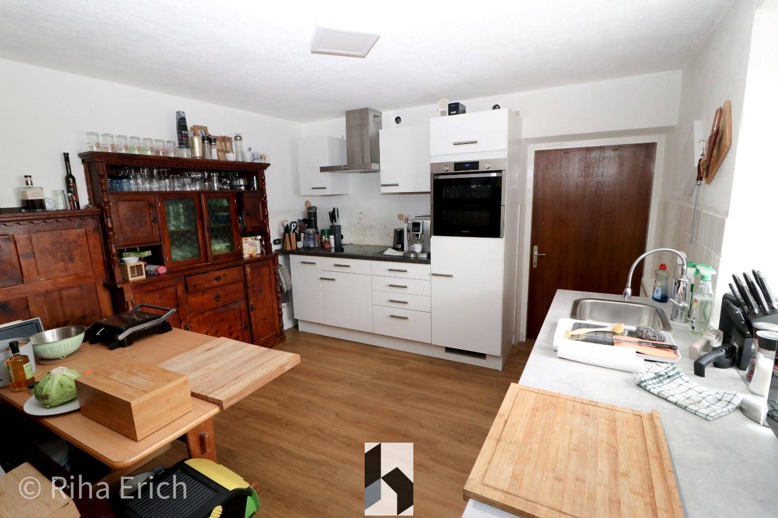 Funktionale Küche mit weißen Schränken, modernen Geräten und traditionellem Holzbuffet, gut ausgestattet.