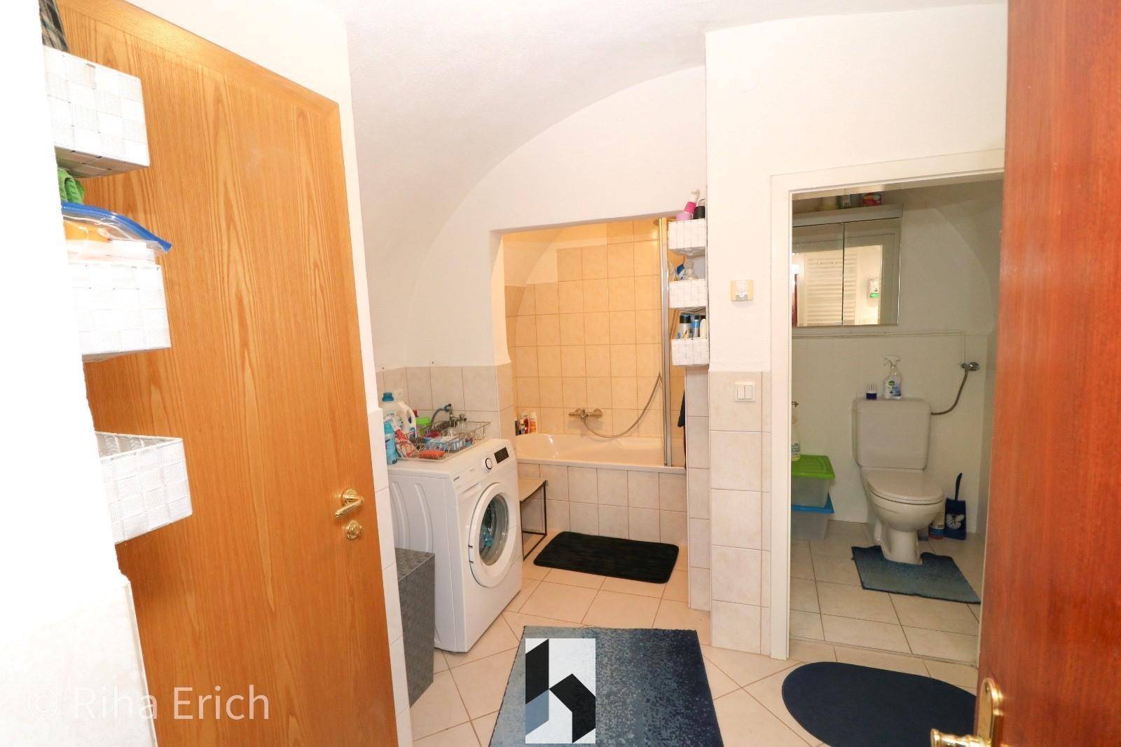 Praktisches Badezimmer mit Badewanne, integrierter Dusche und Waschmaschine, mit separatem WC-Bereich.