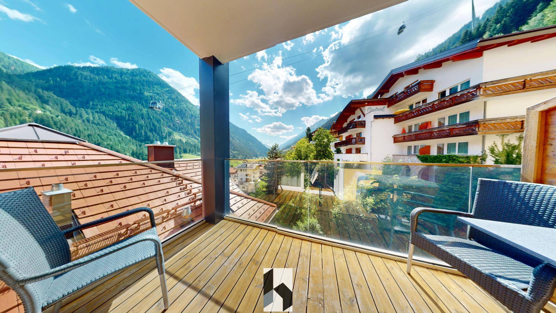 Geräumiger Balkon mit Holzdeck, Glasgeländer und atemberaubendem Panoramablick auf die umliegenden Berge.