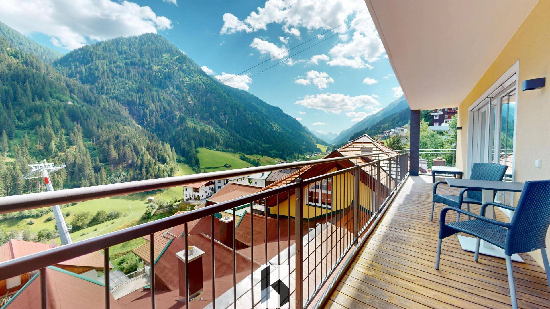 Langer Balkon mit Holzdeck und Sitzgelegenheiten, bietet einen weiten Blick über das Tal und die Berglandschaft.