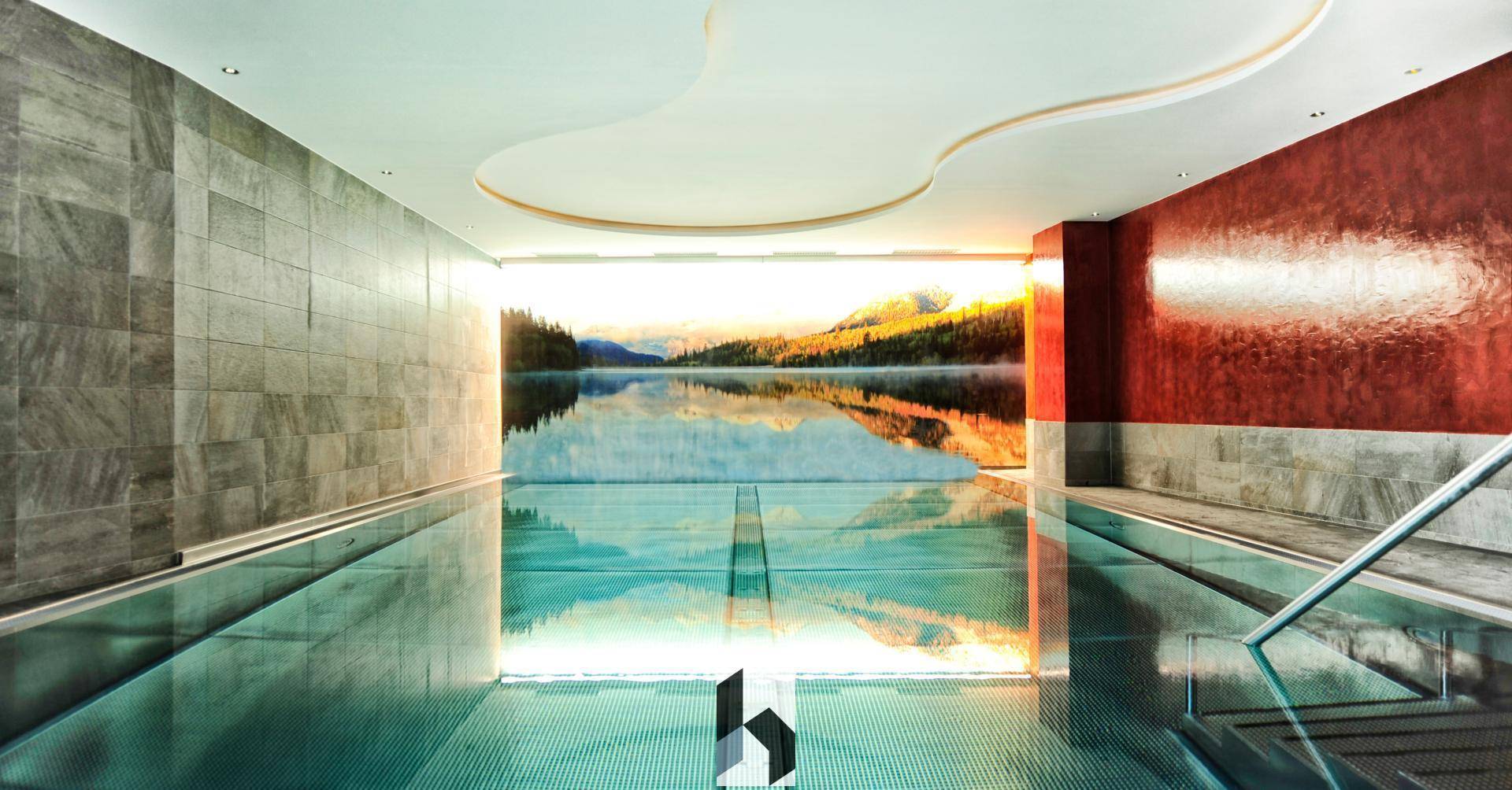 Elegantes Hallenbad mit einem beeindruckenden Wandbild einer Bergseenlandschaft und moderner Beleuchtung.