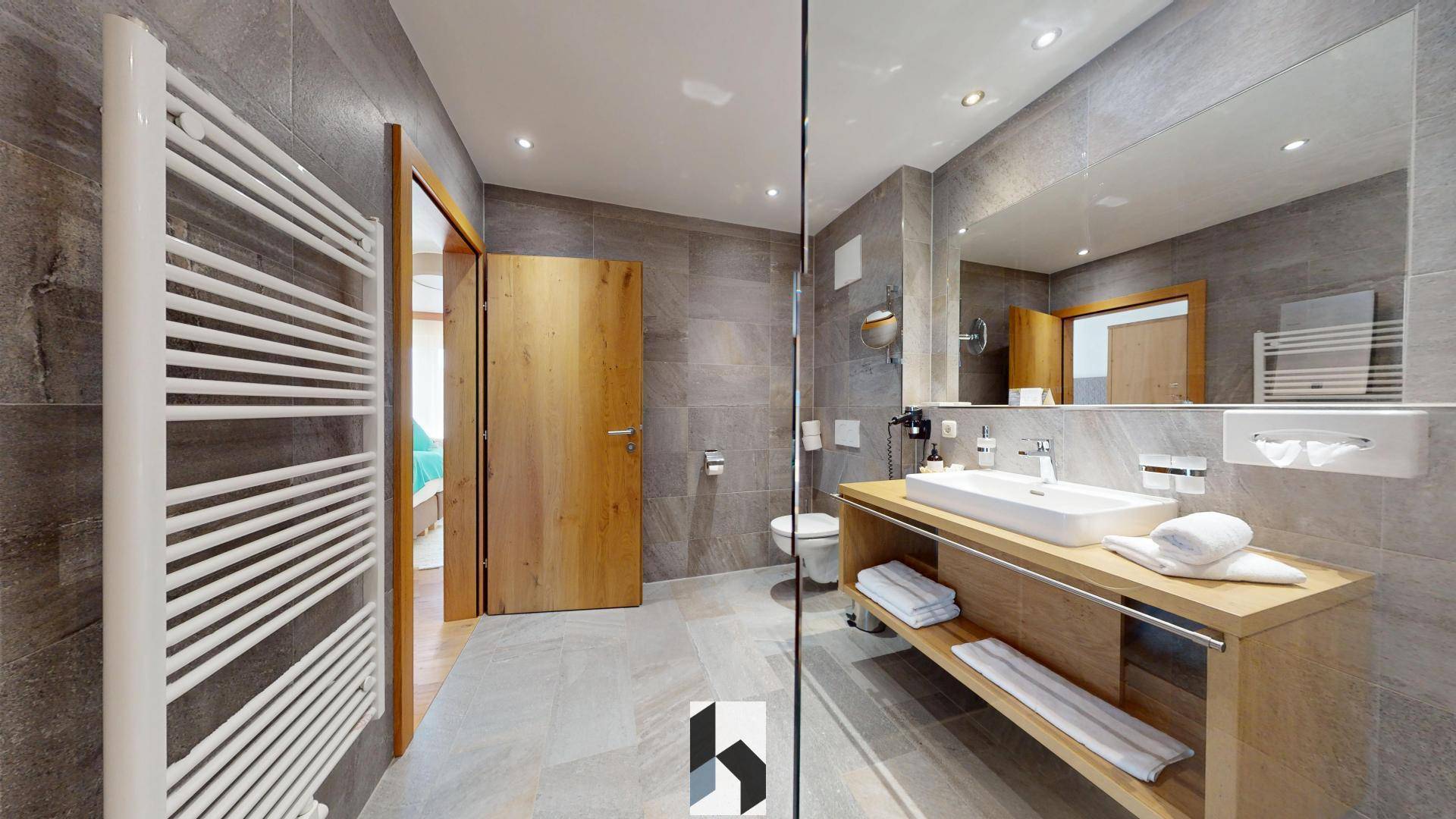 Modernes Badezimmer mit grauen Fliesen, Einzelwaschbecken, begehbarer Dusche und beheiztem Handtuchhalter.