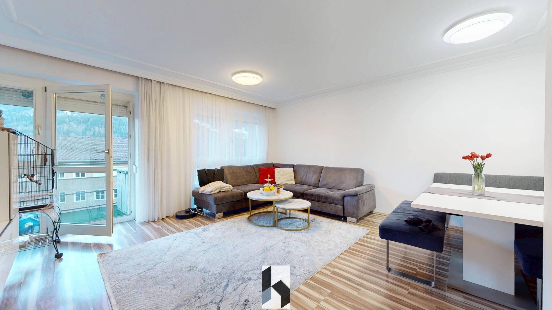 Heller Wohn- und Essbereich mit modernem Sofa, Teppich und Zugang zu einem Balkon.