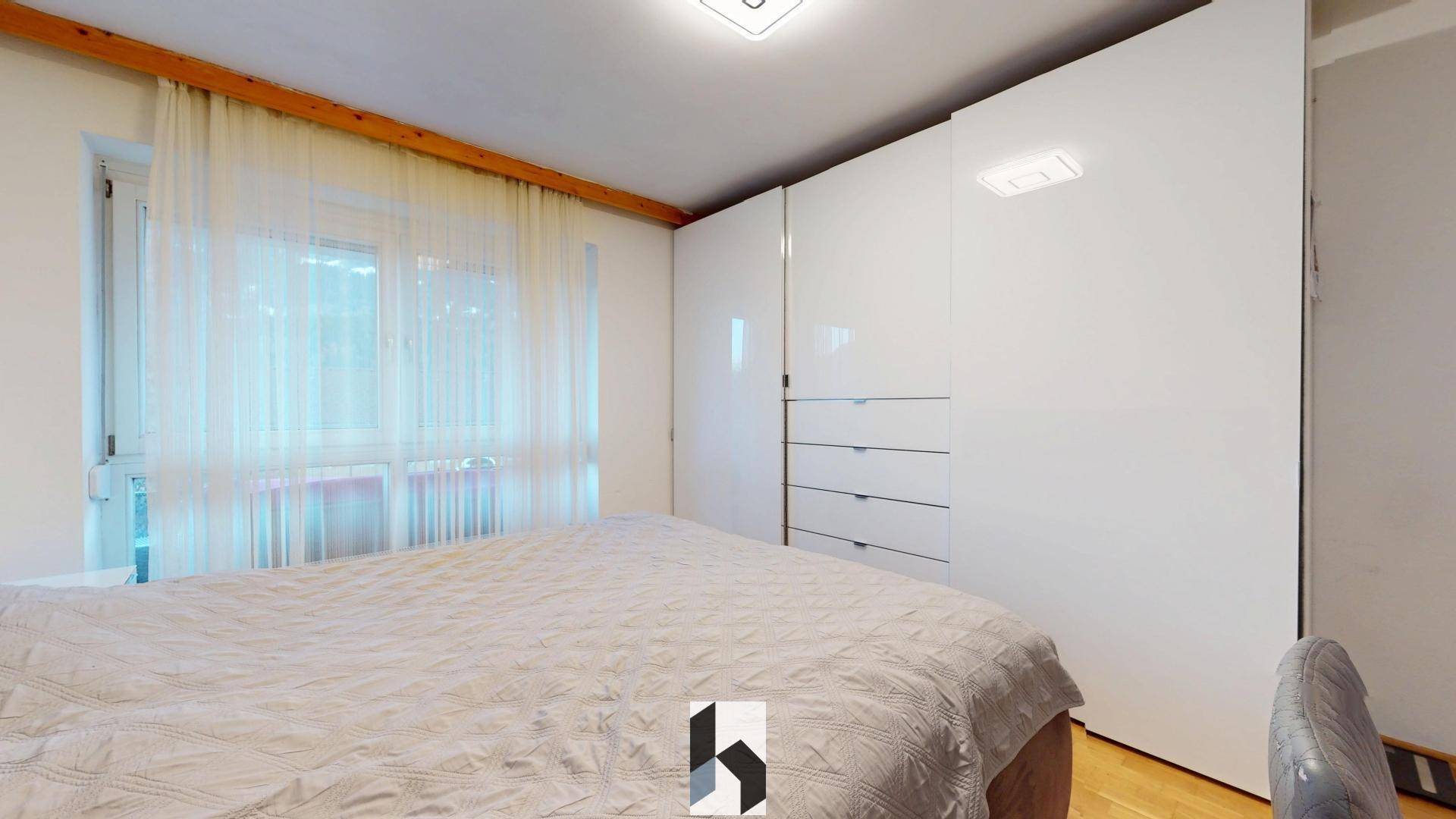 Schlafzimmer mit großem Bett, weißen Einbauschränken und Fenster mit hellen Vorhängen.