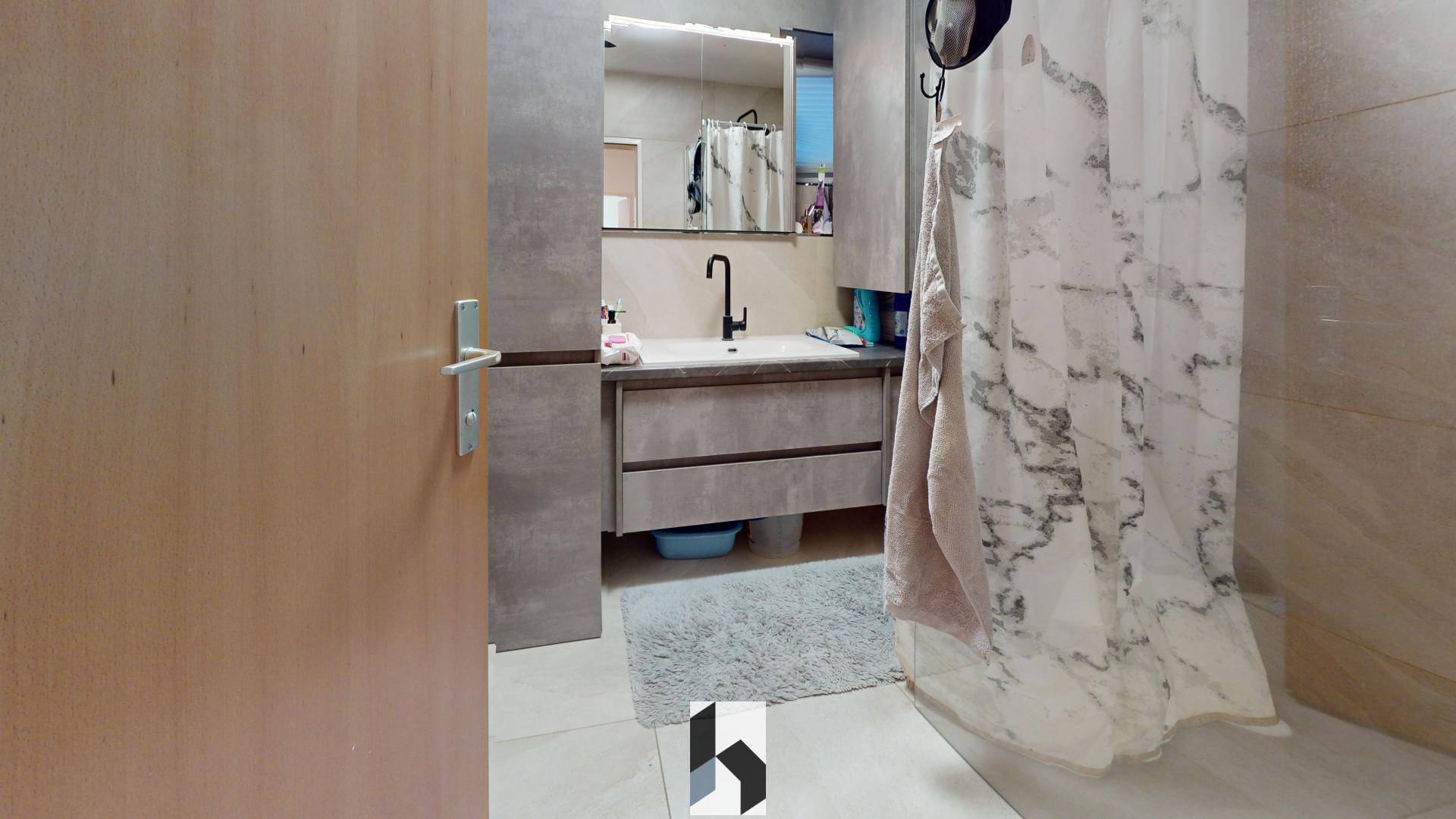 Modernes Badezimmer mit Waschtisch, Spiegel und Duschvorhang in hellen, neutralen Farbtönen.