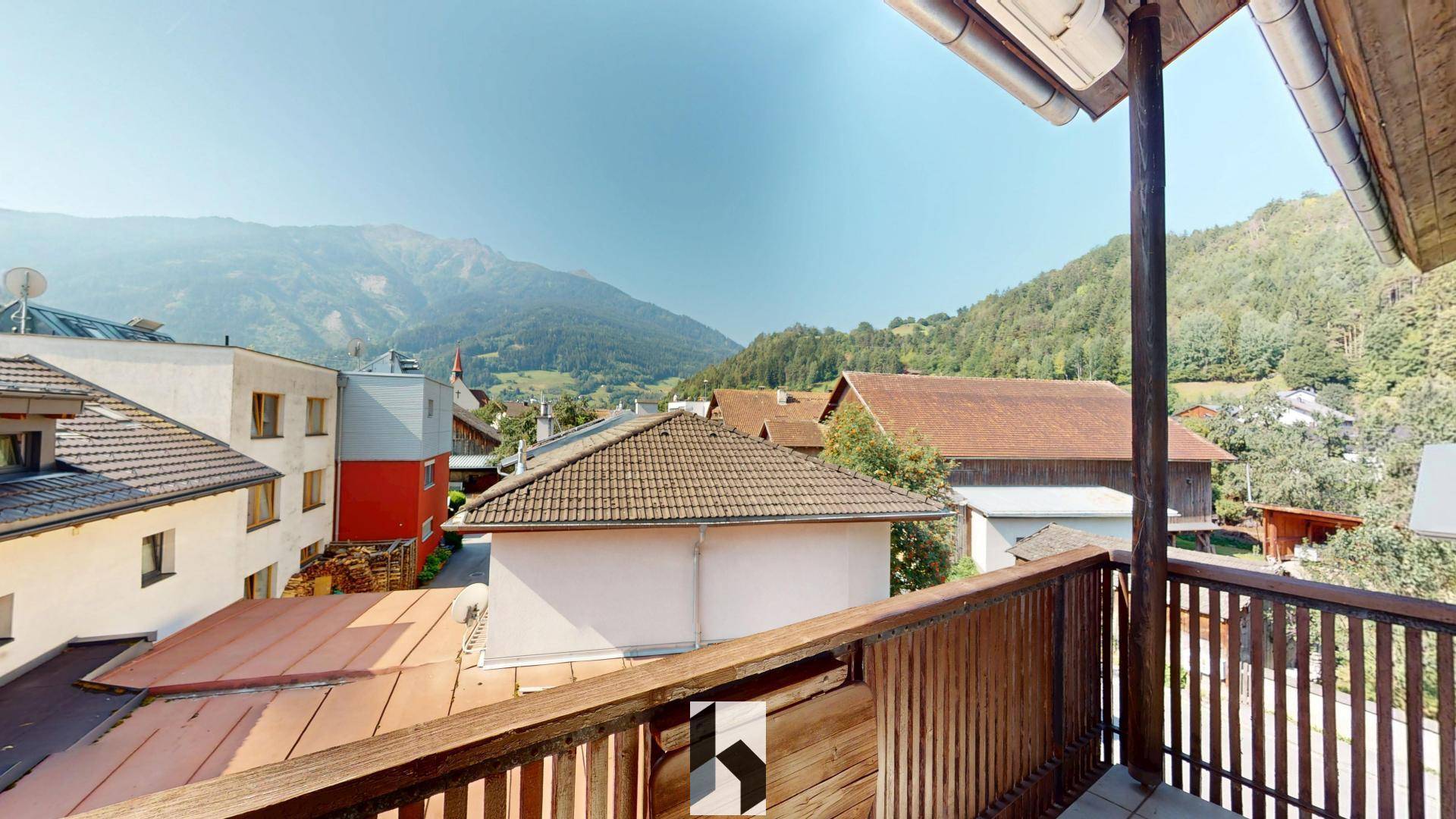 Balkon mit Holzelementen und weitem Blick auf die umliegenden Berge und Dächer.