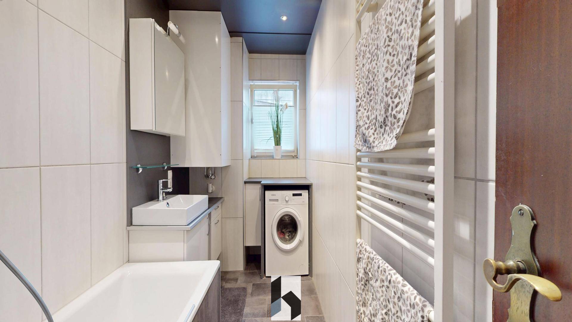 Funktionales Badezimmer mit Badewanne, Waschbecken, Fenster und integrierter Waschmaschine.