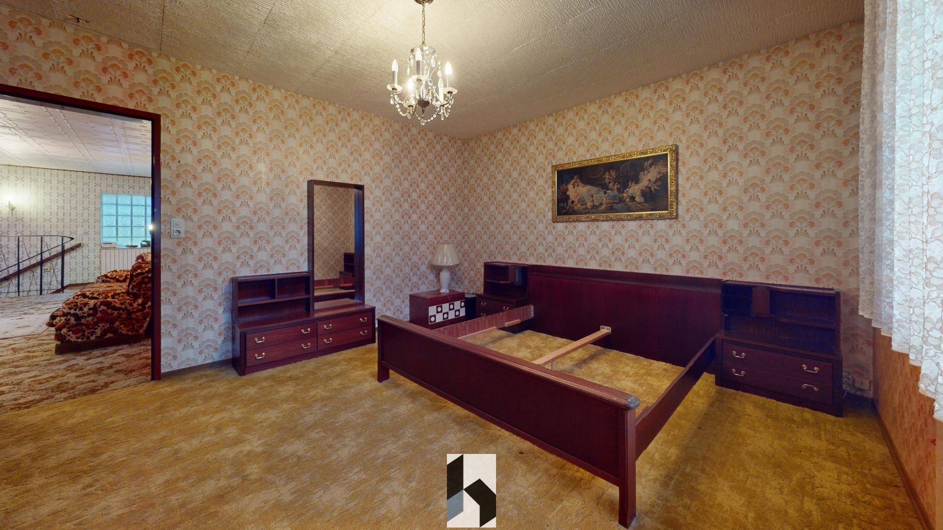 Schlafzimmer mit gemusterter Tapete, Teppichboden und einem großen Holzbettrahmen.