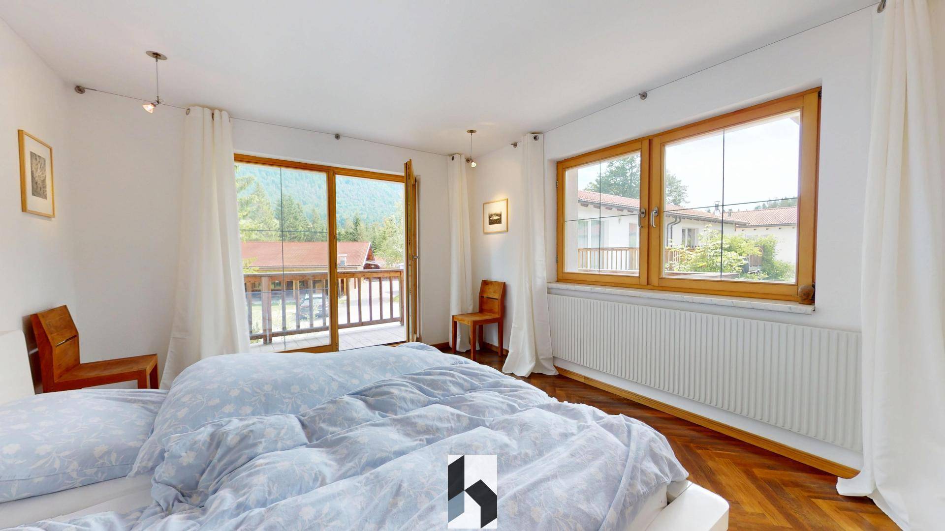 Schlafzimmer mit Holzboden, großem Bett und Balkonzugang mit Blick auf die Umgebung.