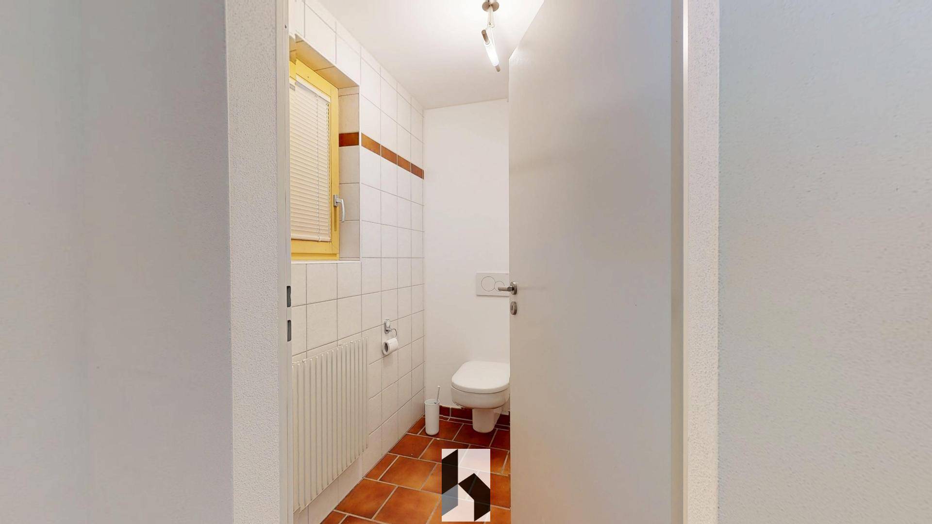 Kleines Gäste-WC mit weißen Fliesen, Fenster und Terrakotta-Bodenfliesen.