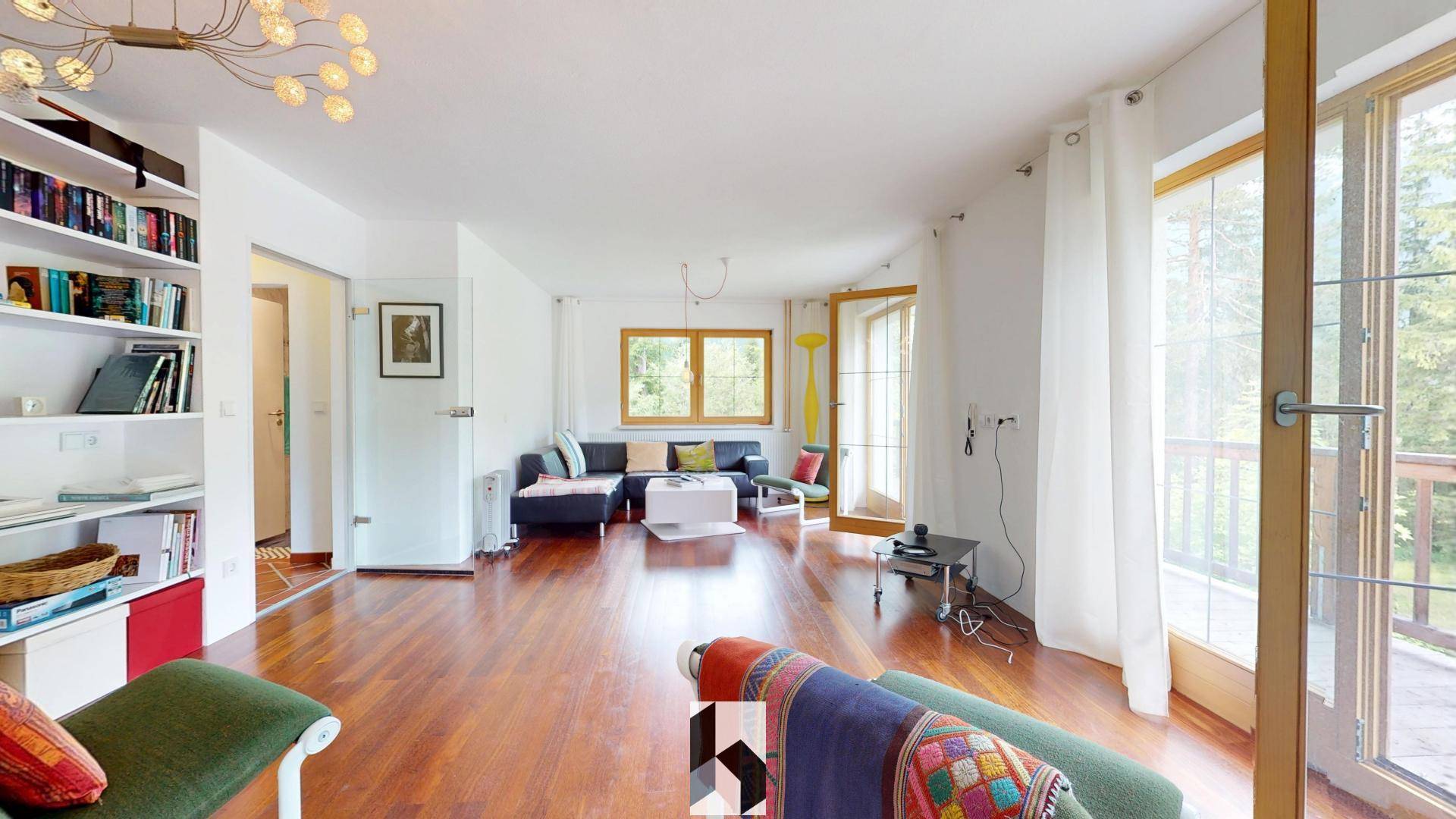 Geräumiges Wohnzimmer mit Holzboden, Bücherregal und Zugang zu einem Balkon mit Aussicht.