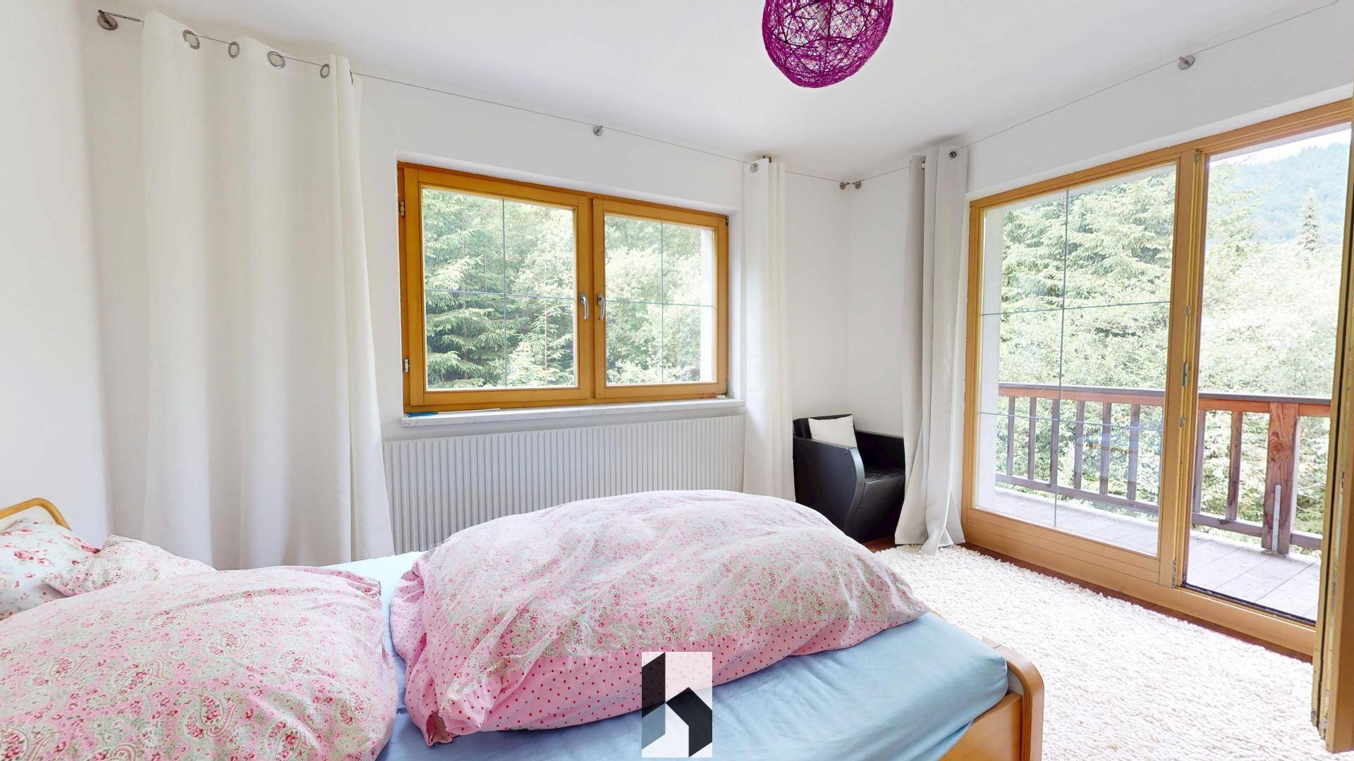 Helles Schlafzimmer mit Teppichboden, großem Fenster und Balkonzugang mit Waldblick.