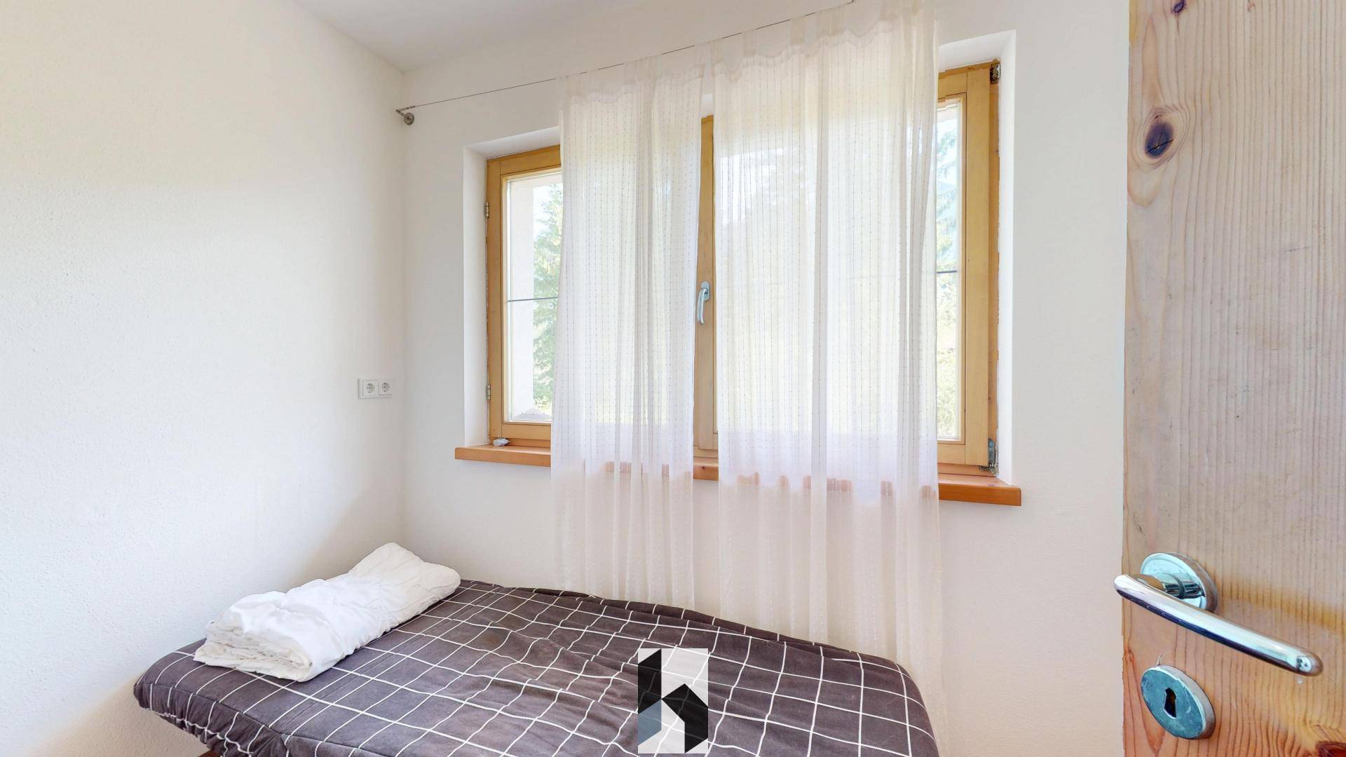 Gemütliches Schlafzimmer mit Einzelbett, hellen Wänden und zwei Fenstern für Tageslicht.